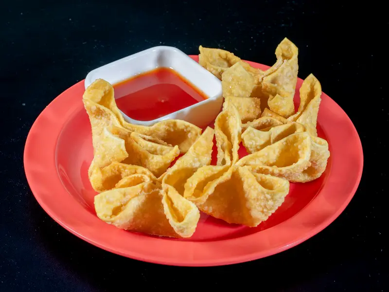 Five crab rangoon on a red plate with sweet chili sauce